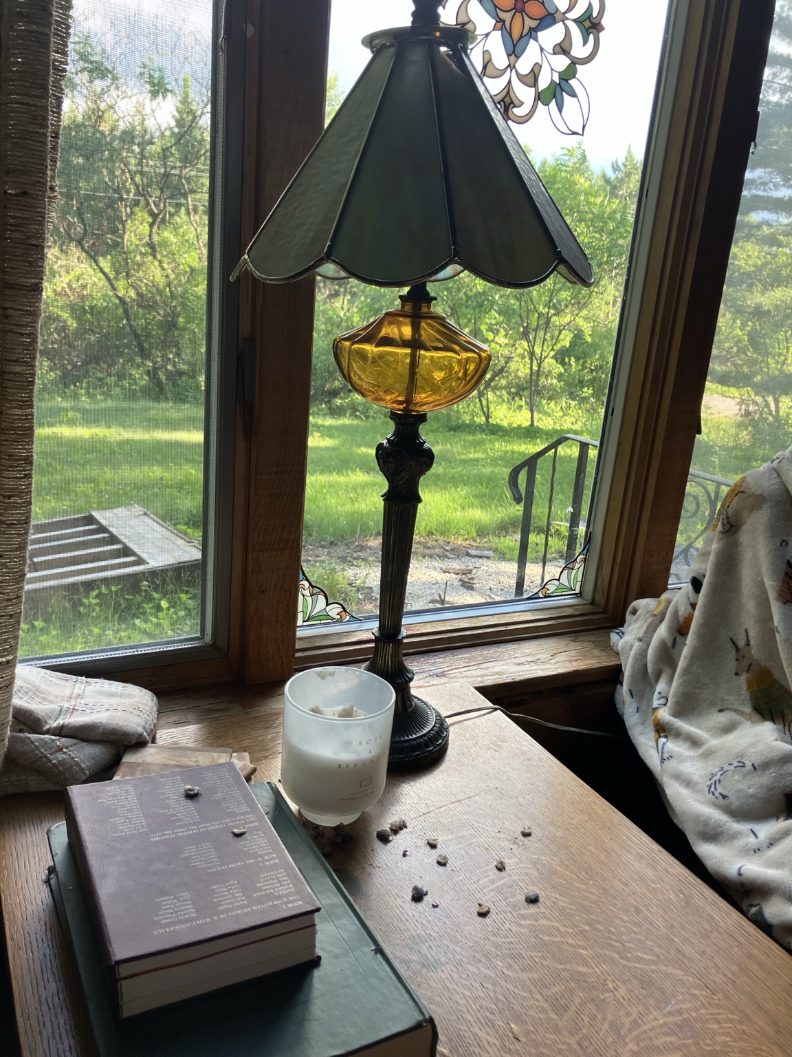 A stained glass lamp beside old books on a sunlit windowsill