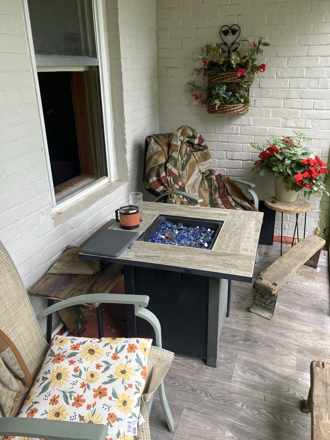 A porch with fire table, blanket, chairs, and a coffee mug